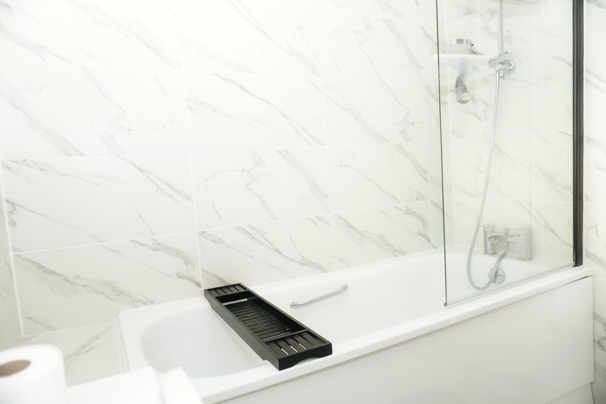 Ein modernes Badezimmer mit einer weißen Badewanne, einer Duschkabine aus Glas und Wänden mit Marmoroptik.