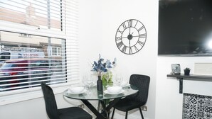A dining area with a round glass table, black chairs, a clock, and a TV. - 3 Bed-sleeps 7-garden-parking-town Centre (Dartford)