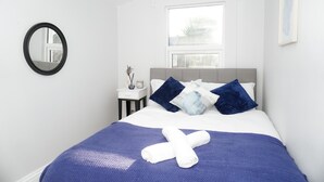 A neatly made bed with a blue bedspread, white pillows, and a rolled white towel. - 3 Bed-sleeps 7-garden-parking-town Centre (Dartford)
