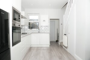 Et moderne køkken med hvide skabe, en indbygget ovn og et vindue over vasken.