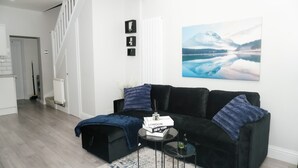 A modern living room with a black sofa, a coffee table, and a painting of a lake. - 3 Bed-sleeps 7-garden-parking-town Centre (Dartford)