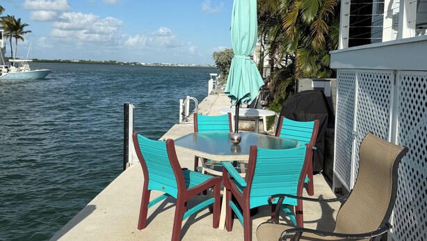 A patio with outdoor furniture, a table, and chairs, overlooking a body of water with a boat in the distance. - Canal front with open water views in Venture Out - Lot 529 (Cudjoe Key)