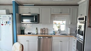 A modern kitchen with white cabinets, stainless steel appliances, and a wooden dining table with a chair. - Canal front with open water views in Venture Out - Lot 529 (Cudjoe Key)