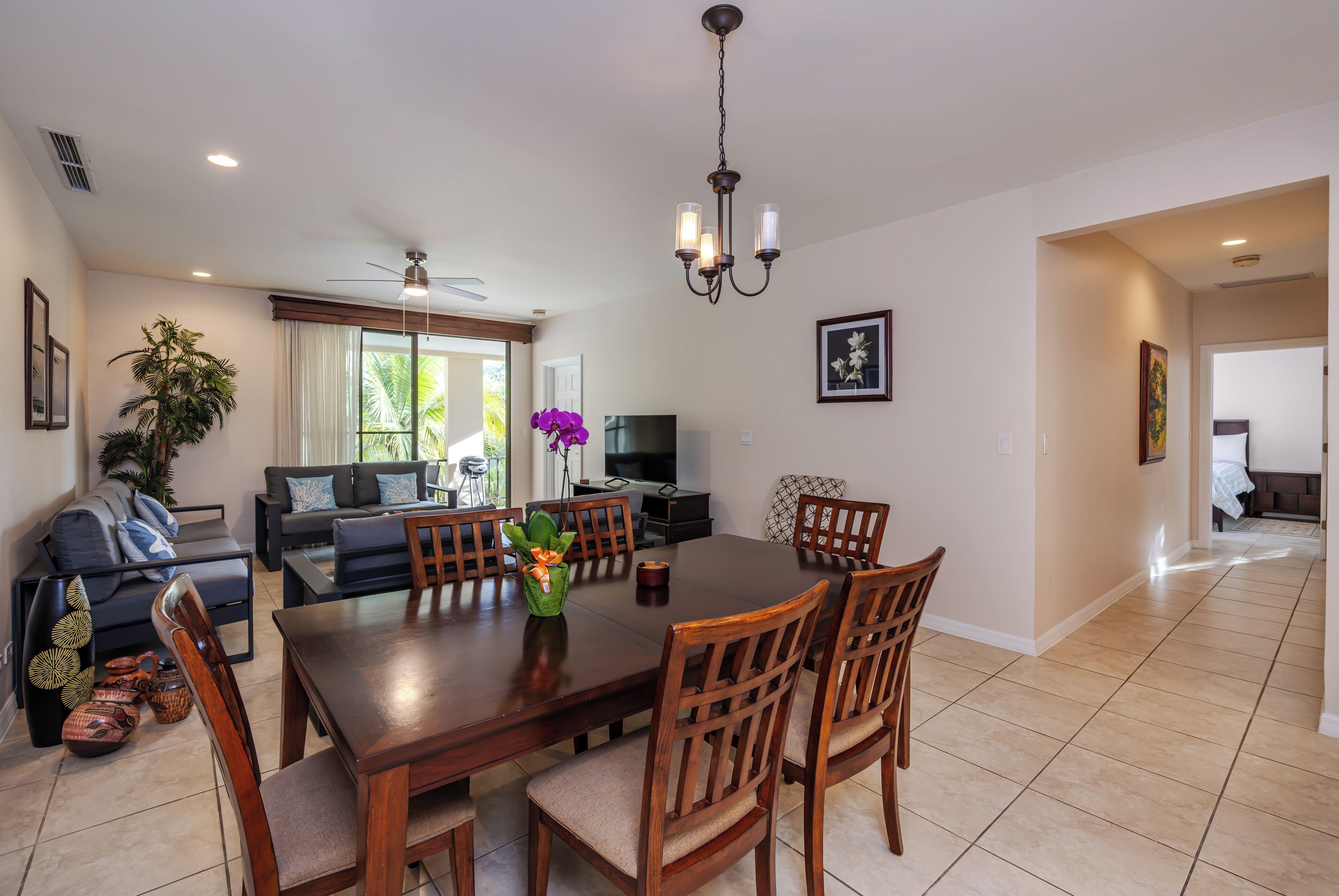 A spacious dining area with a wooden table and chairs, a chandelier, and a large window with curtains.