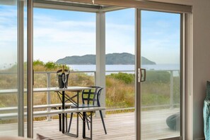 Ein Balkon mit Tisch und Stühlen, der auf ein Gewässer und eine entfernte Insel Blick bietet.
