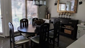 A dining area with a round table, six chairs, a chandelier, a mirror, and a cabinet with decorative items.