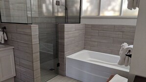 A modern bathroom with a glass shower enclosure, a white bathtub, and a wooden stool.