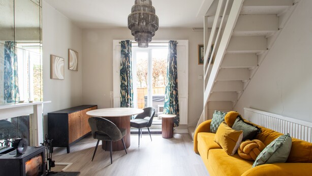 Ein modernes Wohnzimmer mit einem gelben Sofa, einer Essecke mit einem runden Tisch und einem Kamin.
