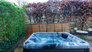 Ein Whirlpool in einem Garten mit Holzzaun, Tisch und Stühlen.