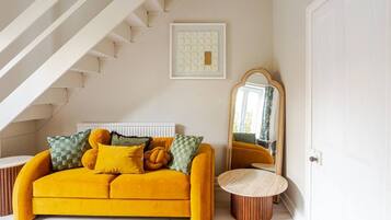 A room with a yellow sofa, a mirror, a framed artwork, and a staircase.