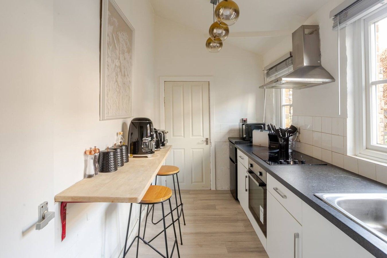 A kitchen with a wooden countertop, bar stools, a coffee machine, and a window with a view.