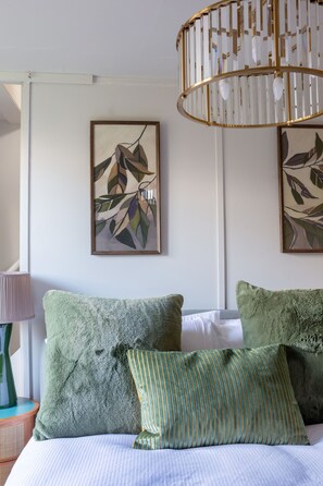 Une chambre à coucher avec un lit, des oreillers verts, un oreiller à rayures, une lampe et deux œuvres d’art encadrées accrochées au mur.