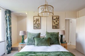 A bedroom with a bed, two nightstands, a chandelier, and artwork on the wall.