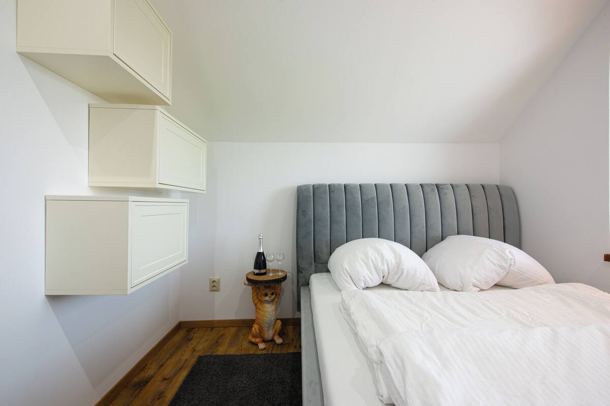 A bedroom with a bed, a nightstand, a wall-mounted cabinet, and a small wooden stool.