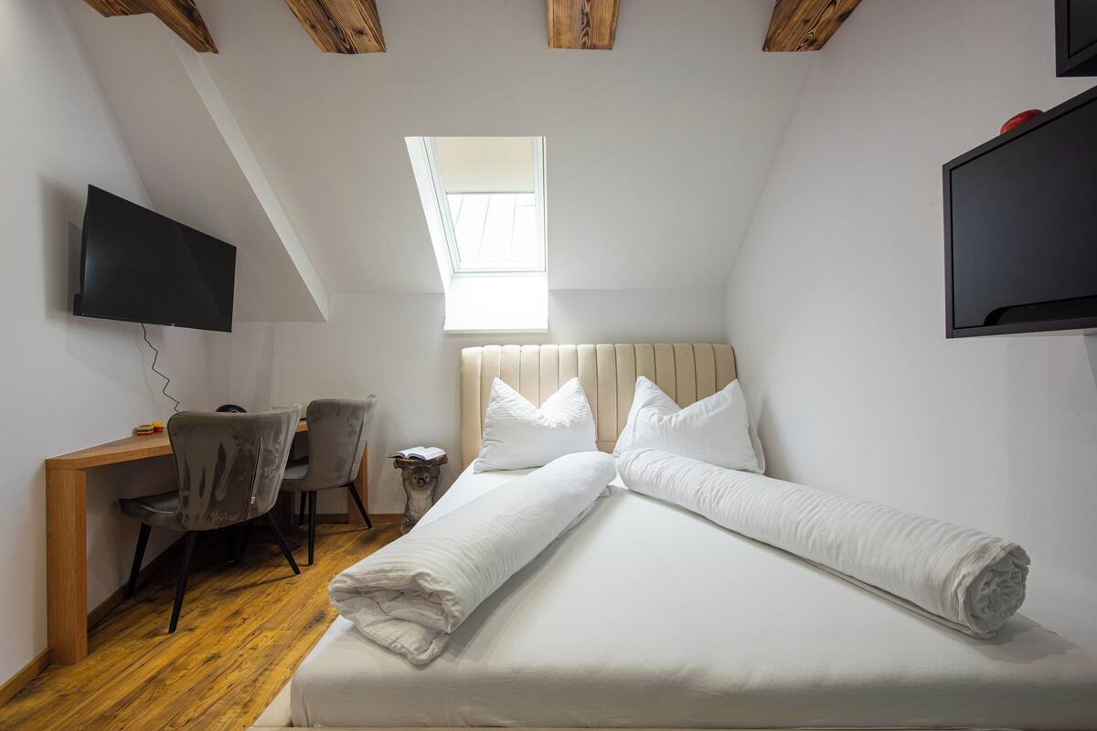 A bedroom with a bed, a desk, two chairs, a TV, and a skylight.