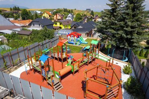 Ein Spielplatz mit verschiedenen Spielgeräten, umgeben von Häusern und einem großen Baum.