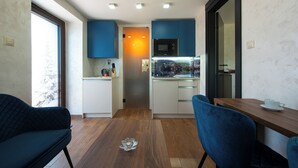 A compact kitchen with blue cabinets, a wooden dining table, and a blue chair. - Apartmány Žakovce & SPA (Vysoké Tatry)