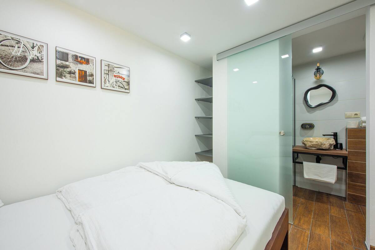 A modern hotel room with a bed, a bathroom with a mirror, and three framed pictures on the wall.