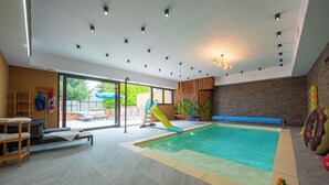 An indoor swimming pool with a slide, lounge chairs, and a view of the outdoors. - Apartmány Žakovce & SPA (Vysoké Tatry)