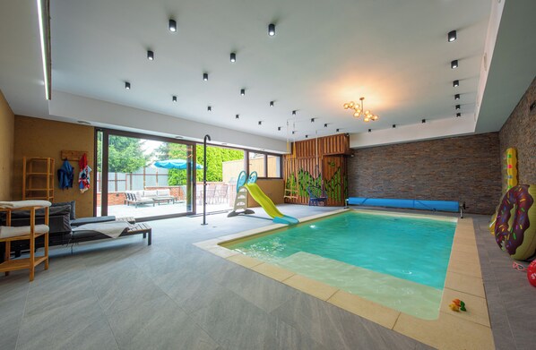 An indoor swimming pool with a slide, lounge chairs, and a view of the outdoors.