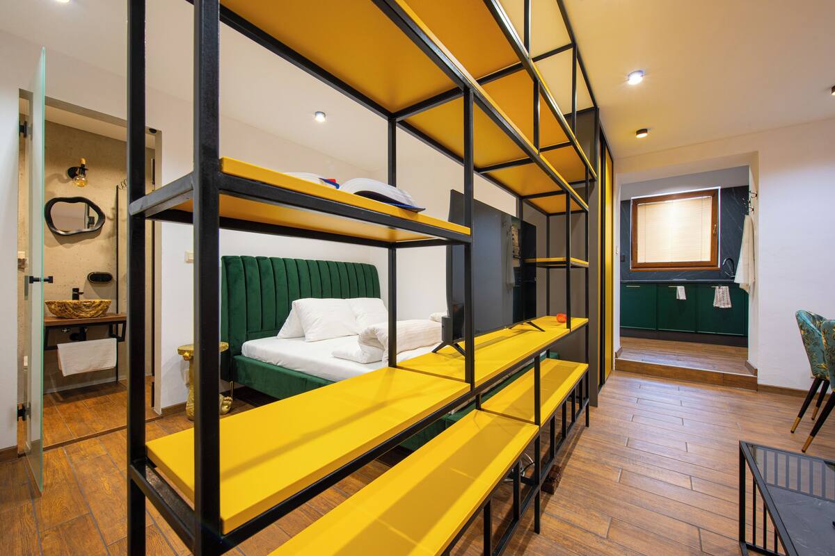 A bunk bed with a green headboard and white bedding, a yellow bench, and a wooden floor.