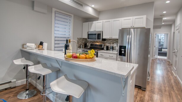 Una cocina moderna con armarios blancos, electrodomésticos de acero inoxidable y una isla central con taburetes de bar.