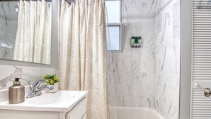 Un baño con lavamanos de mármol blanco, un espejo, una cortina de ducha y una bañera.