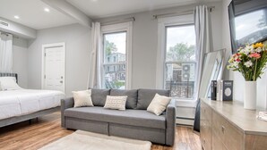 Un dormitorio moderno con un sofá gris, una cama blanca y un ventanal con cortinas.