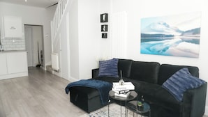 Ett modernt vardagsrum med en svart soffa, ett soffbord och en tavla som föreställer ett berglandskap.