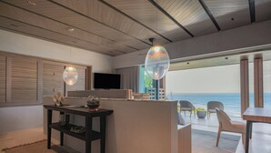 A modern living room with a wooden ceiling, a TV, a dining area with chairs, and a view of the ocean.