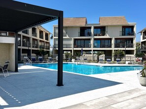A hotel with a swimming pool, outdoor seating, and a covered area.