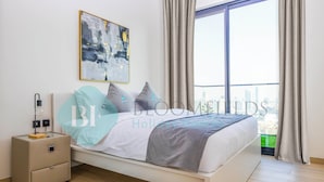 A modern bedroom with a bed, bedside table, and a large window with curtains. - Bloomfields 1Br Binghatti Heights (Dubai)