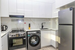 A compact kitchen with a gas stove, a washing machine, a refrigerator, and a sink. - Bloomfields 1Br Binghatti Heights (Dubai)