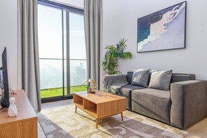 A modern living room with a sofa, a coffee table, a TV, and a large window with curtains. - Bloomfields 1Br Binghatti Heights (Dubai)