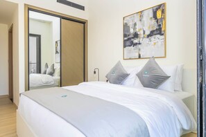 A modern hotel room with a large bed, a sliding door closet, a wall-mounted abstract painting, and a bedside lamp. - Bloomfields 1Br Binghatti Heights (Dubai)