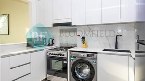 A modern kitchen with white cabinets, a gas stove, an oven, and a built-in washing machine. - Bloomfields 1Br Binghatti Heights (Dubai)