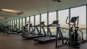 A gym with treadmills and elliptical machines, large windows, and a view of buildings. - Bloomfields 1Br Binghatti Heights (Dubai)