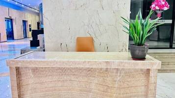 A reception desk with a marble top, a potted plant with green foliage, and a pink flower arrangement.