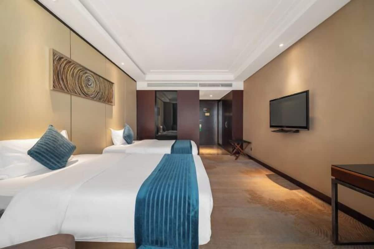 Una habitación de hotel con dos camas, un televisor y un pasillo que conduce a otra habitación.