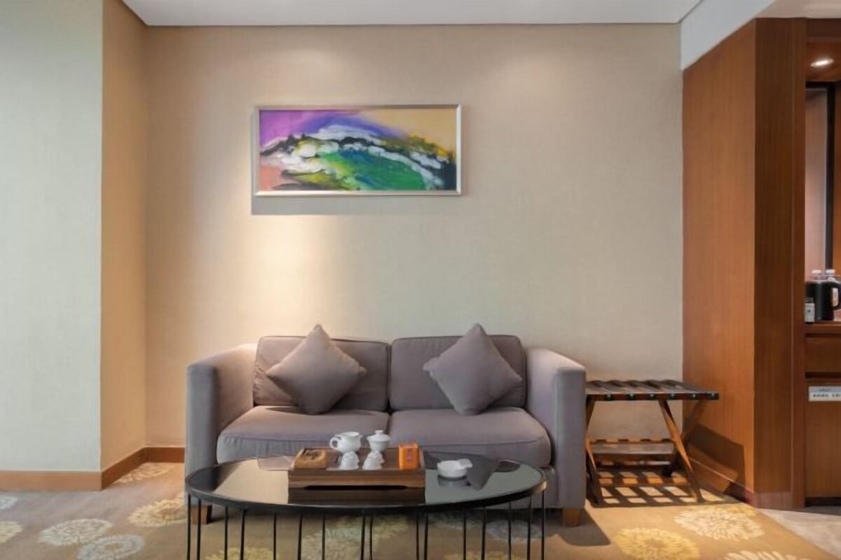 Un salon moderne avec un canapé gris, une table basse sur laquelle se trouve un plateau avec du thé et des tasses, et un tableau accroché au mur.