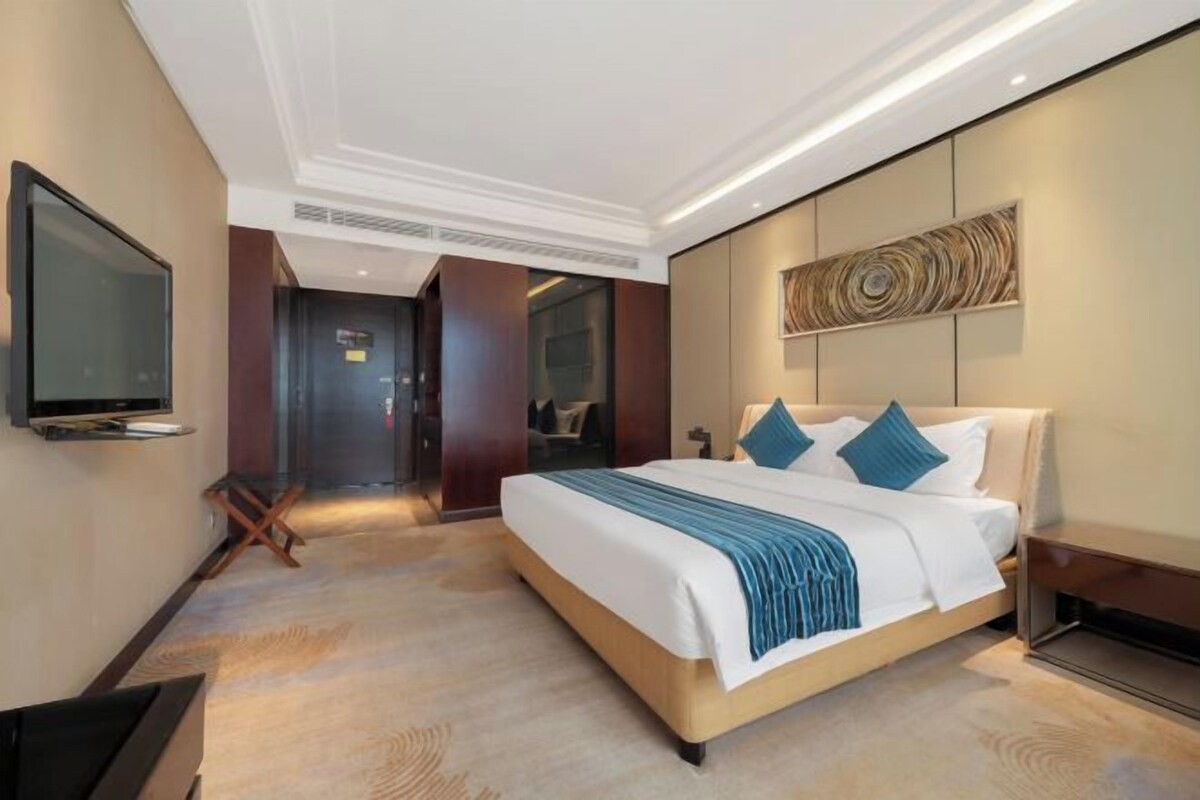 Une chambre d’hôtel comprenant un lit, un téléviseur à écran plat, une œuvre d’art accrochée au mur et une porte donnant sur une autre pièce.