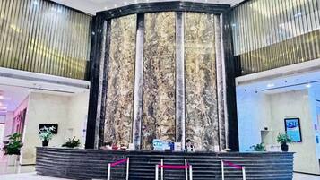 Un área de recepción con una pared de mármol, un mostrador de recepción y una escalera que conduce a plantas superiores.