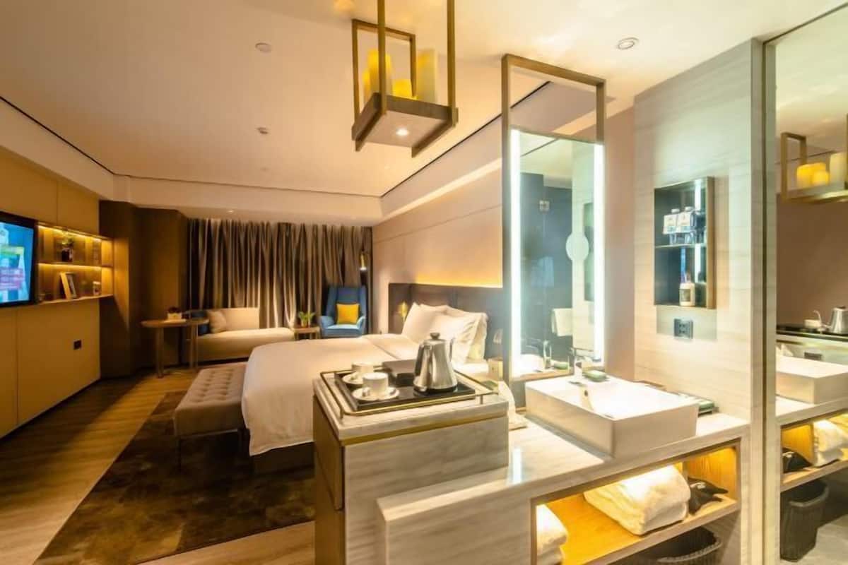 Habitación de hotel con cama, mesitas de noche, televisor, espejo y baño con lavamanos y espejo.
