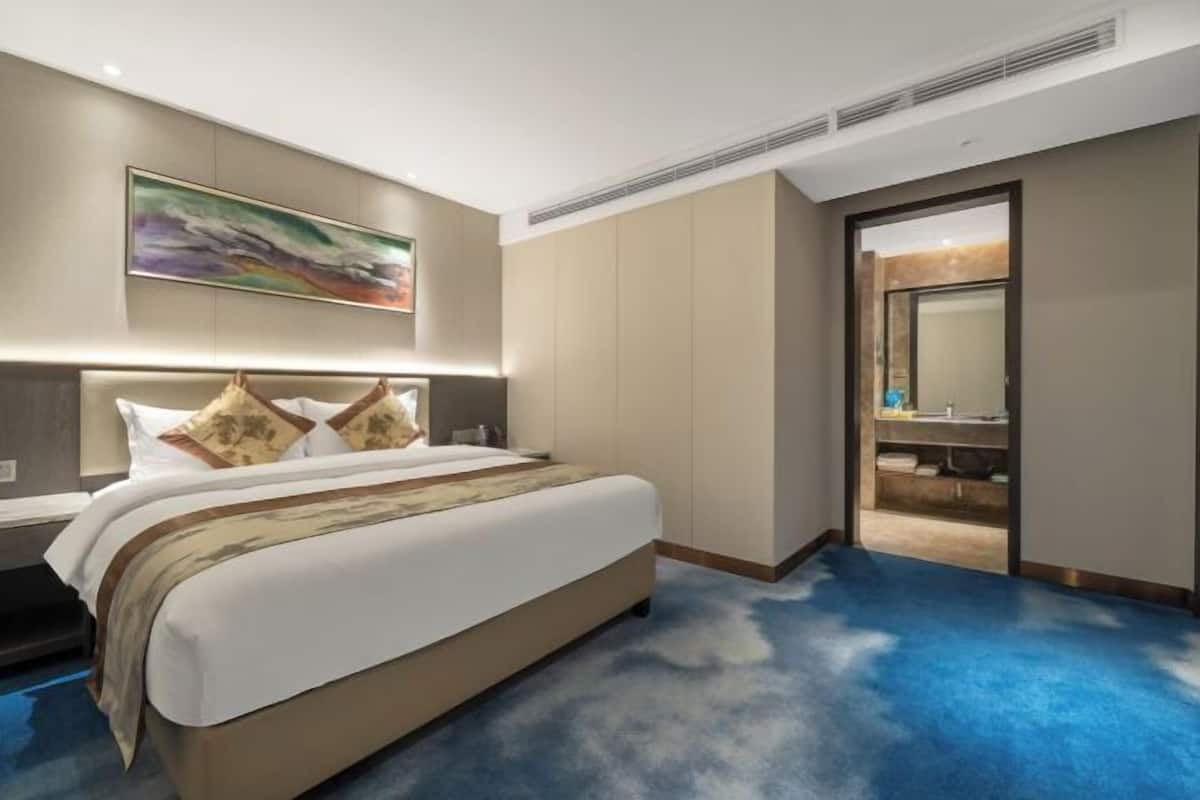 Habitación de hotel moderna con una cama grande, un cuadro en la pared y vistas al baño.