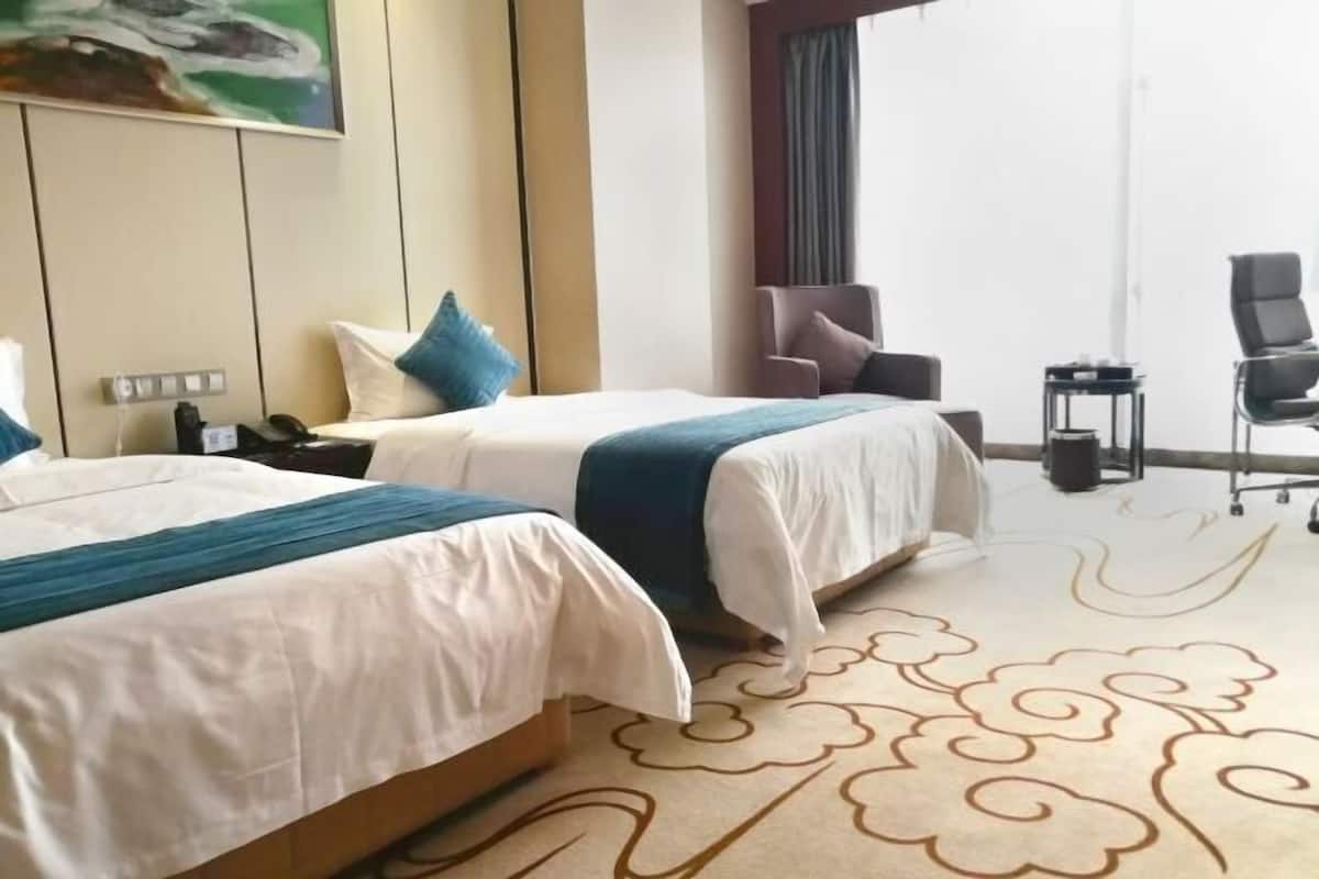 Habitación de hotel con dos camas, un escritorio, una silla y un ventanal grande.