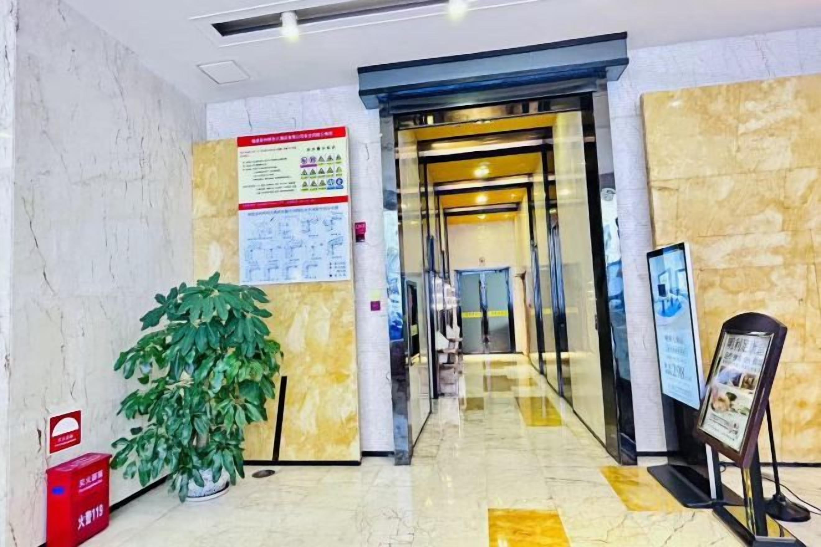 Un vestíbulo de hotel con piso de mármol, una recepción, una planta en maceta y un cartel en la pared.