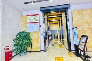 A hotel lobby with a marble floor, a reception desk, a potted plant, and a poster on the wall. - Minlff Hotel (Quanzhou)
