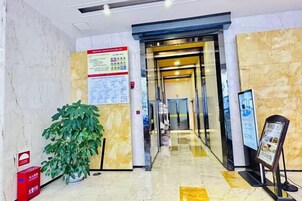 Un vestíbulo de hotel con piso de mármol, una recepción, una planta en maceta y un cartel en la pared.