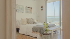 A bedroom with a bed, a bench, a potted plant, and a view of the beach. - Condominio frente al mar  Morros Epic. (Cartagena)