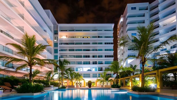 A modern hotel with a pool, palm trees, and a well-lit facade. - Condominio frente al mar  Morros Epic. (Cartagena)